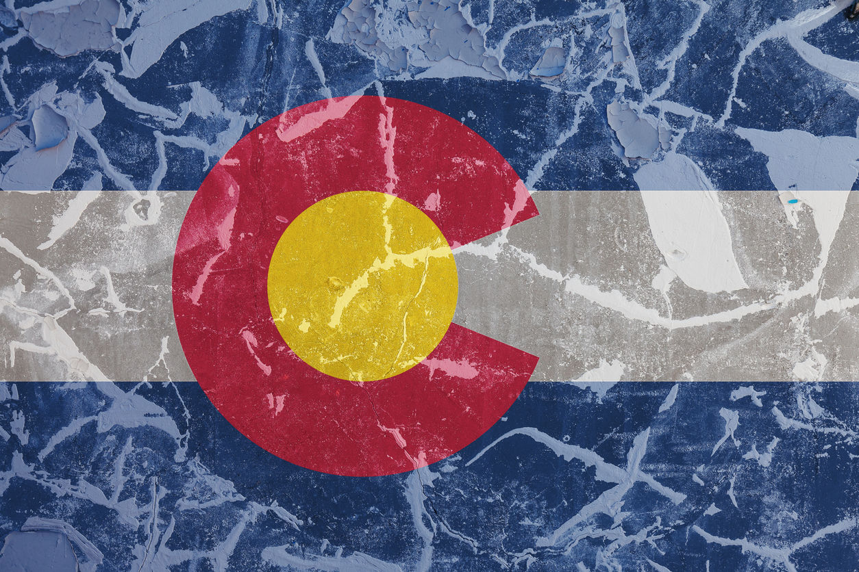 The national flag of the US state Colorado in against a gray wall with cracks and faults on the day of independence in blue red and yellow. Political and religious disputes, customs and delivery.
